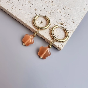 Gros plan de boucles d'oreilles dorées avec pendentifs fleurs sur un support en pierre