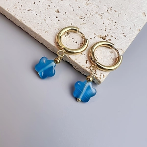 Détail macro de boucles d'oreilles fleurs dorées avec pendentifs étoiles bleues sur pierre