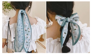 Détail d'un foulard étroit en soie bleu clair à fleurs, noué et suspendu avec élégance