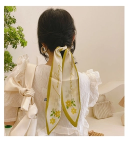 Détail d'un foulard en soie noué aux cheveux, beige et vert olive avec des fleurs jaunes