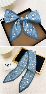 Détail d'un foulard en soie bleu étroit avec motifs nœuds blancs et bords contrastés