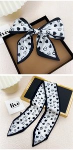 Détail de l'élégant foulard en soie à motif de cœurs noir et blanc noué en nœud décoratif