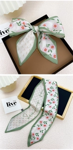 Détail d'un foulard long en soie avec motifs géométriques verts et fleurs roses
