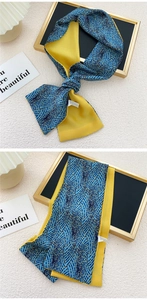 Détail d'un foulard étroit en soie montrant des motifs de vagues bleu-or et un revers jaune