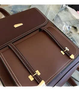 Detail of deep brown PU leather backpack with contrasting white stitching and gold buckles