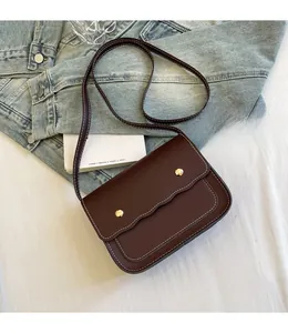 Detail of dark brown PU leather crossbody bag with white stitching and gold buckles