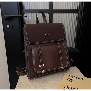 Detail of dark reddish-brown vintage backpack with white contrast stitching and gold buckles