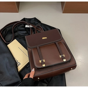 Detail view of deep brown leather backpack with contrast stitching and golden buckles