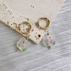 Detailed close-up of gold stainless steel hoop earrings with floral glass pendants