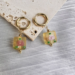 Detail of gold hoop earrings with amber glass square charms and pink rose inlay