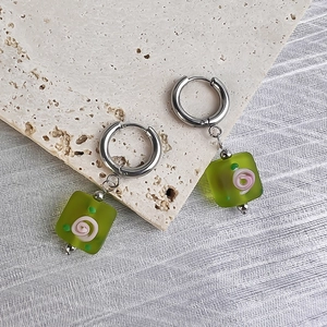 Detail of square green resin earrings with pink floral patterns on stone surface