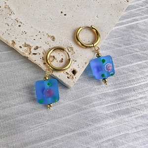 Detail of vintage gold hoop earrings with blue square resin pendants and floral patterns