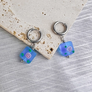 Detail of blue square glass earring with purple rose pattern on travertine stone