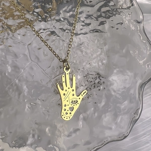 Detail showing an 18K gold Hamsa Hand pendant with hollow heart and eye engravings