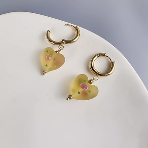Detail of heart-shaped glass earrings with frosted rose pattern on gold hoops