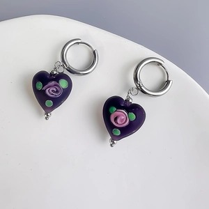 Close-up of heart-shaped purple glass earrings with pink rose detail on a white ceramic plate
