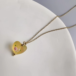 Détail d'un collier pendentif cœur en verre mat avec volutes roses et chaîne dorée