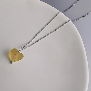 Détail du pendentif cœur en verre dépoli avec spirales roses sur chaîne en acier