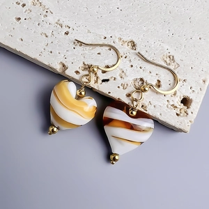 Close-up of heart-shaped resin earrings with striped patterns on a minimalist stone base
