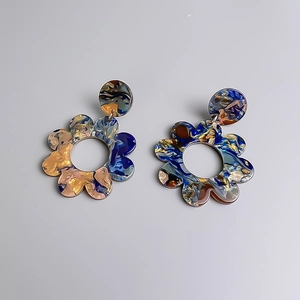 Dettaglio di orecchini a fiore in acrilico con trama marmorizzata blu e arancione