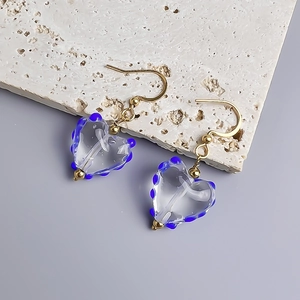 Detailaufnahme von herzförmigen Glasohrringen mit blauen Punkten auf Steinoberfläche