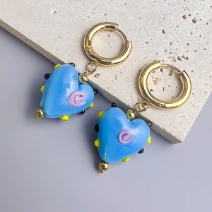 Détail de boucles d'oreilles cœur en résine bleue avec créole dorée sur pierre