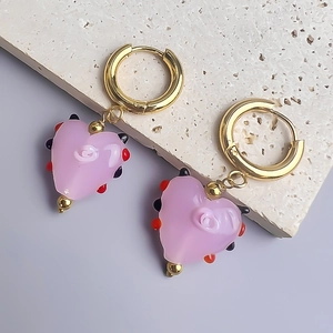 Détail de boucles d'oreilles cœur en verre rose avec spirale et pois sur anneau doré