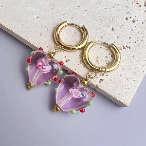 Détail de la boucle d'oreille cœur en verre violet avec motifs tourbillons roses
