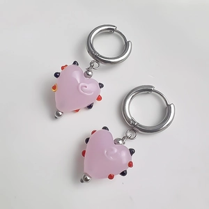 Détail de créoles argentées avec pendentifs en forme de cœur rose et motifs à pois