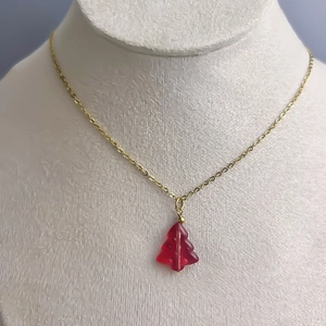 Detail of a gold-plated stainless steel necklace with a red glass Christmas tree pendant