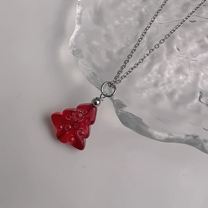 Detailed macro shot of a vibrant red glass Christmas tree pendant on a silver chain necklace