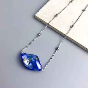 Detailed close-up of dark blue art glass pendant on a thin silver chain with beads