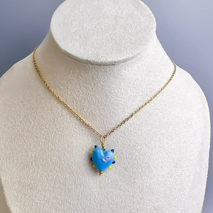Detailweergave van hemelblauwe hartjesketting gedragen op een witte getextureerde buste