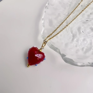 Detail van rode hartvormige hanger met blauwe accenten en goudkleurige ketting
