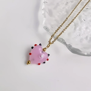 Detailopname van een hartvormige roze glazen hanger aan een gouden ketting met kralen
