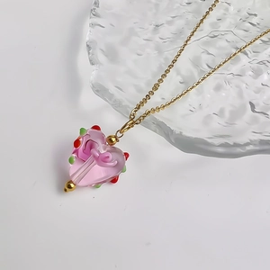 Detail van roze glazen hartvormige hanger aan gouden ketting op een ijsstructuur blad