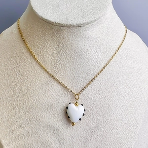Vue détaillée du pendentif cœur avec pois noirs sur une surface en émail blanc