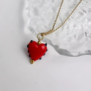 Détail d'un pendentif cœur rouge avec accents dorés sur une fine chaîne en or