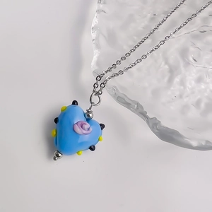 Detailopname van blauwe hartvormige hanger met paarse roos en stippen aan zilveren ketting