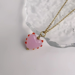 Gros plan d'un pendentif cœur en verre rose avec points rouges sur une chaîne dorée