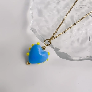 Détail du pendentif cœur en verre bleu avec accents jaunes sur chaîne en acier doré