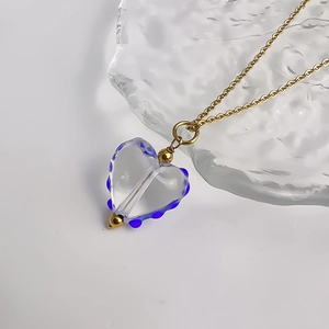 Vue macro du pendentif coeur en verre avec points bleus sur une fine chaîne dorée