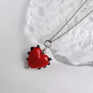 Vue détaillée d'un pendentif cœur en verre rouge sur une fine chaîne en acier inoxydable argenté