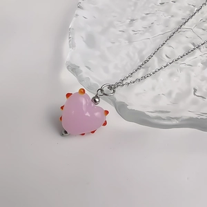Gros plan du pendentif cœur en verre rose avec pointes orange sur chaîne argentée