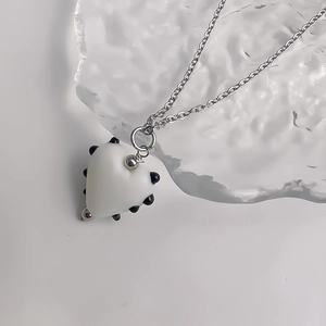 Gros plan détaillé du pendentif cœur blanc à pois noirs sur une chaîne en acier argenté