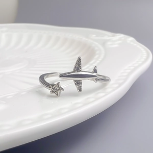 Détail macro d'une bague avion et étoile avec zircons posée sur céramique blanche