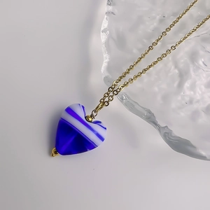 Gros plan détaillé du pendentif cœur en verre rayé bleu et blanc sur une chaîne dorée