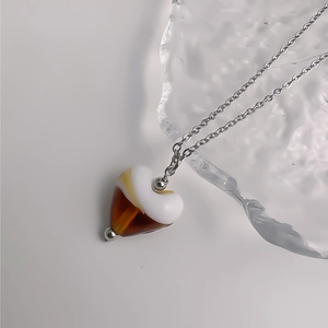 Détail du collier cœur avec pendentif en résine ivoire et ambre sur chaîne argentée