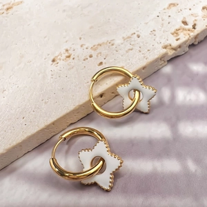 Dettaglio di orecchini a stella in oro 18K con ciondoli in smalto bianco su pietra
