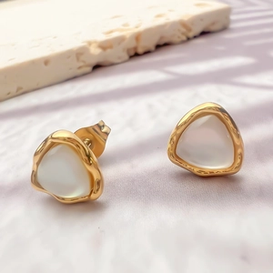 Close-up of triangle cat-eye stud earrings with golden wavy edges on a textured stone
